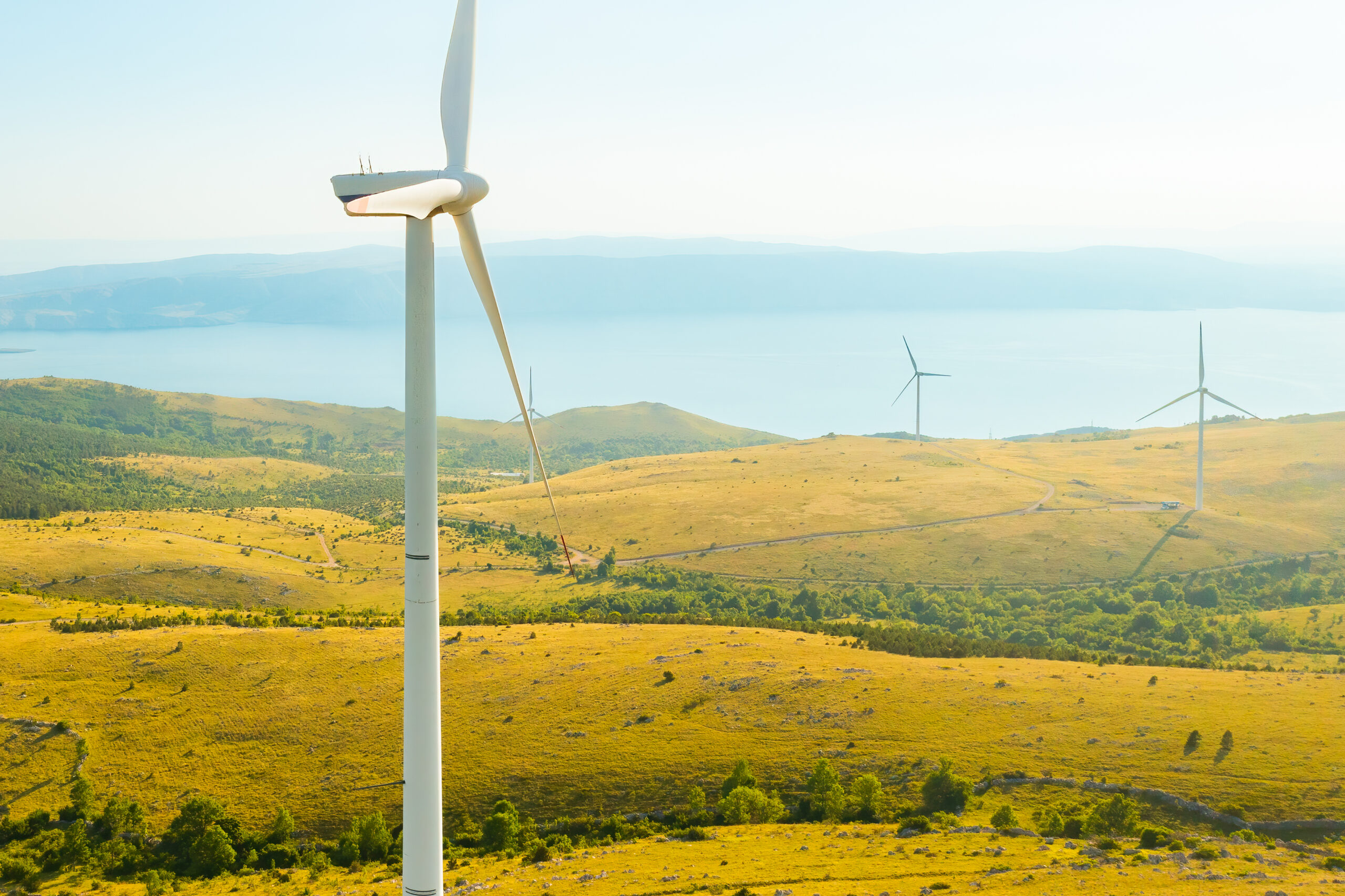 Une éolienne domine un paysage méditérannéen avec la mer en fond