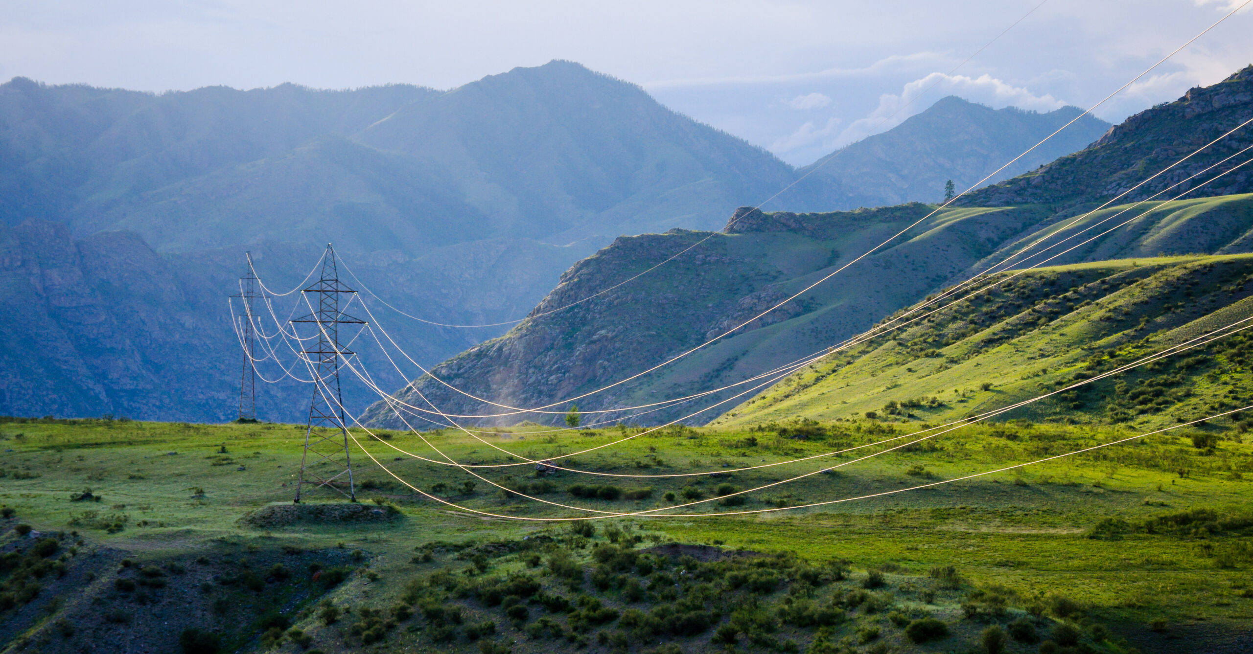 Une ligne électrique haute tension dans un paysage montagneux verdoyant et ensoleillé