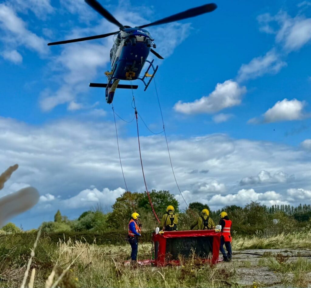 un hélicoptère s'élève pour transporter une calle avec des techniciens qui vont réaliser des travaux sous tension